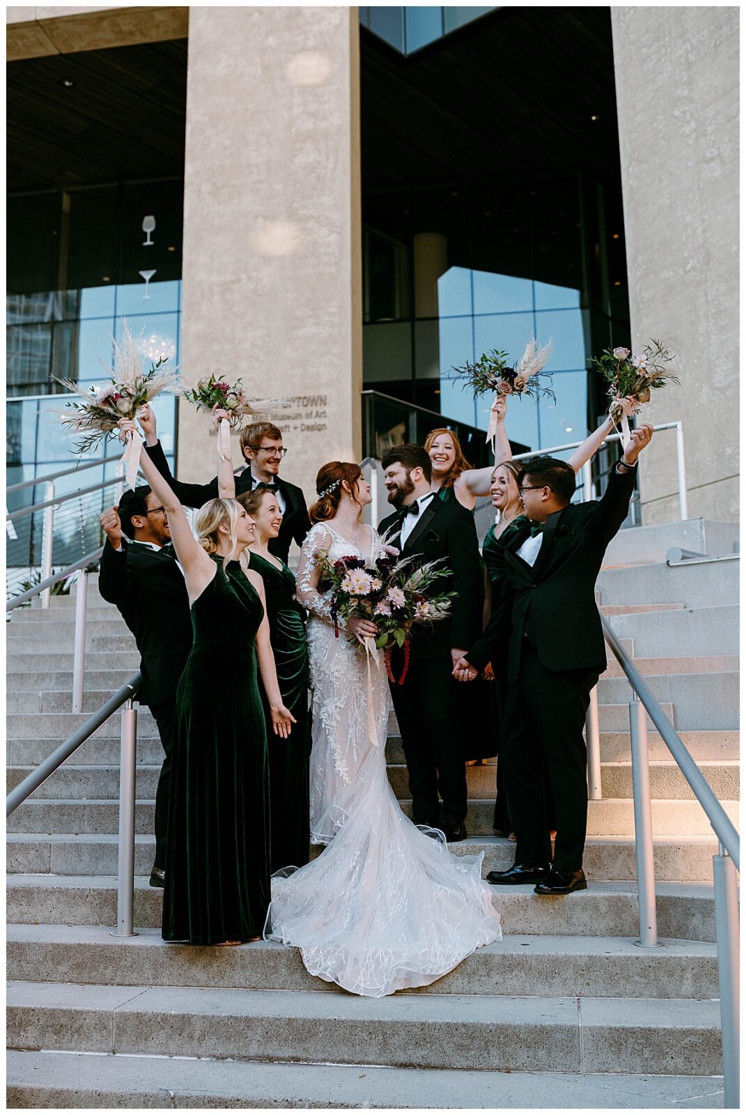 bridal party throws hands in the air on steps of modern art museum
