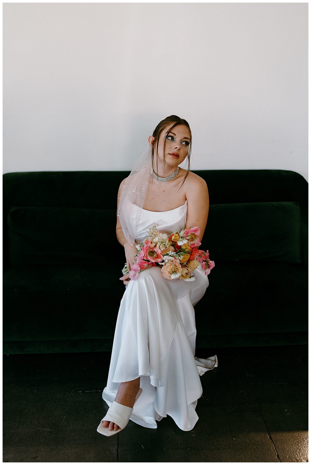 bride looks to side as she sits on couch holding bouquet at Junction West styled shoot