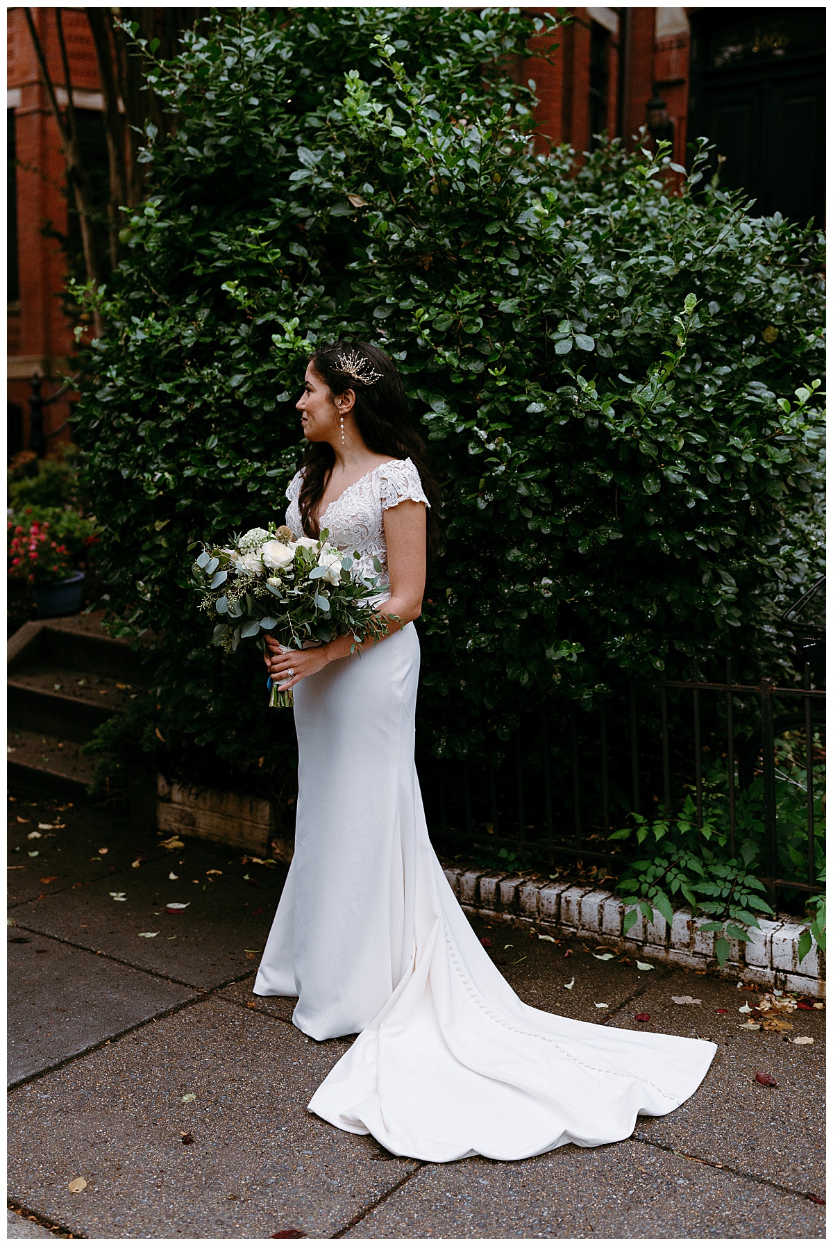 bride holds bouquet and looks to the side in front of greenery by destination wedding photographer