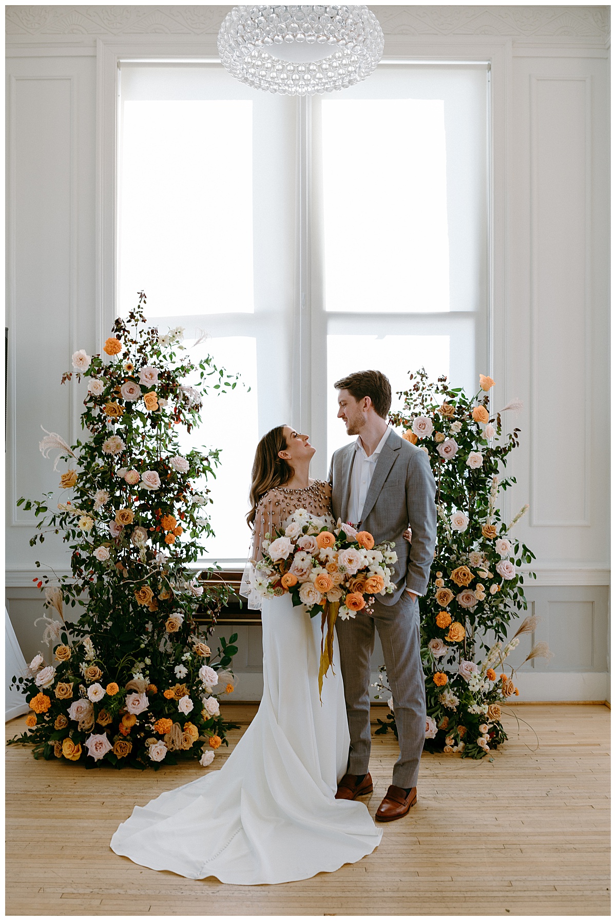 couple looks into each other's eyes in front of floral ceremony arch by The Hazel Club