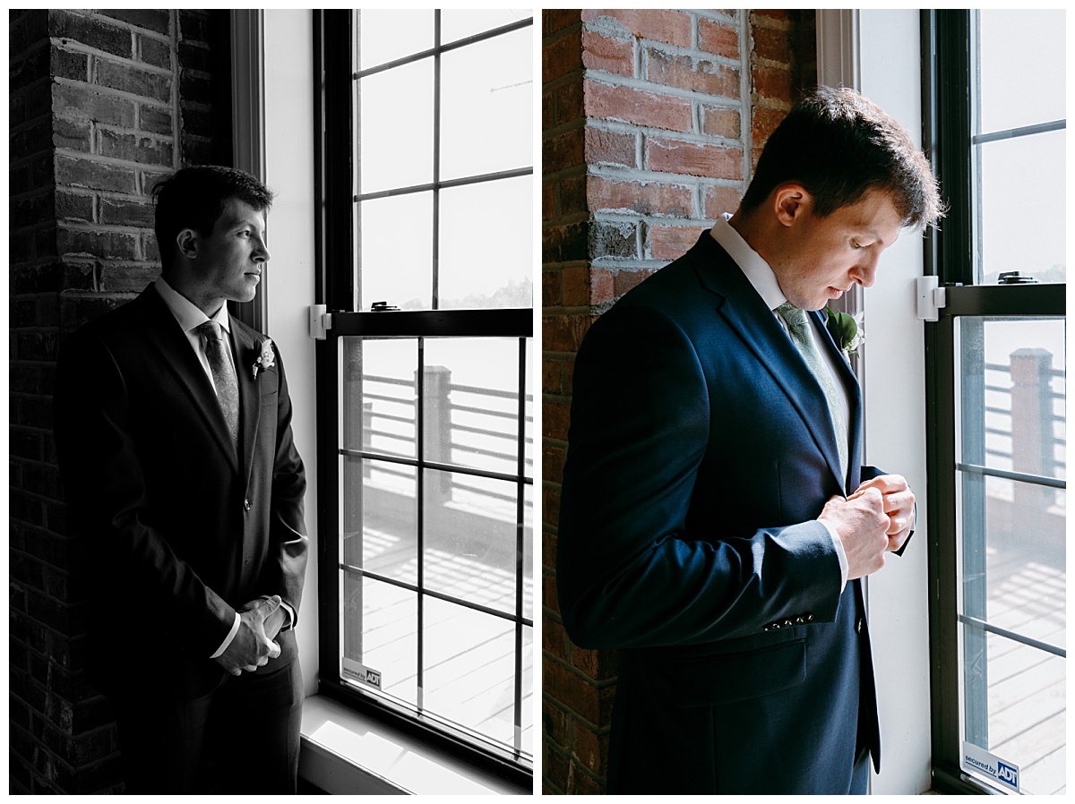 man stands by window looking out and adjusting suit by North Carolina wedding photographer