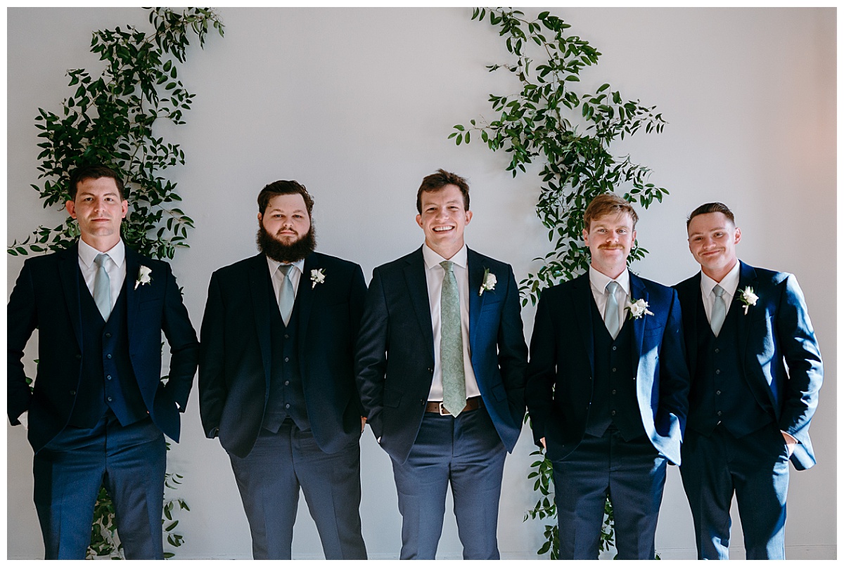 groomsmen stand together under arch at River Room