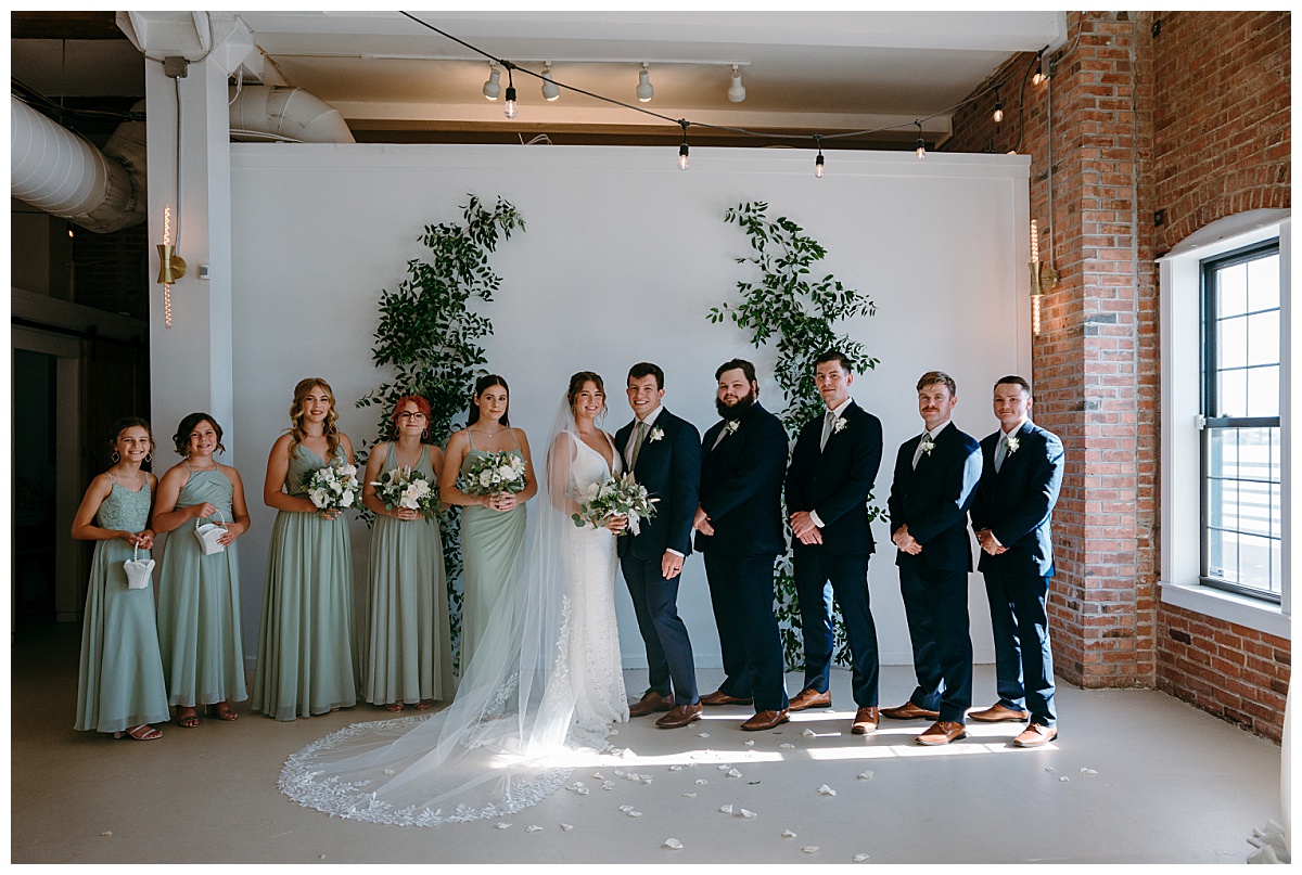 bridal party stands together under ceremony arch by North Carolina wedding photographer
