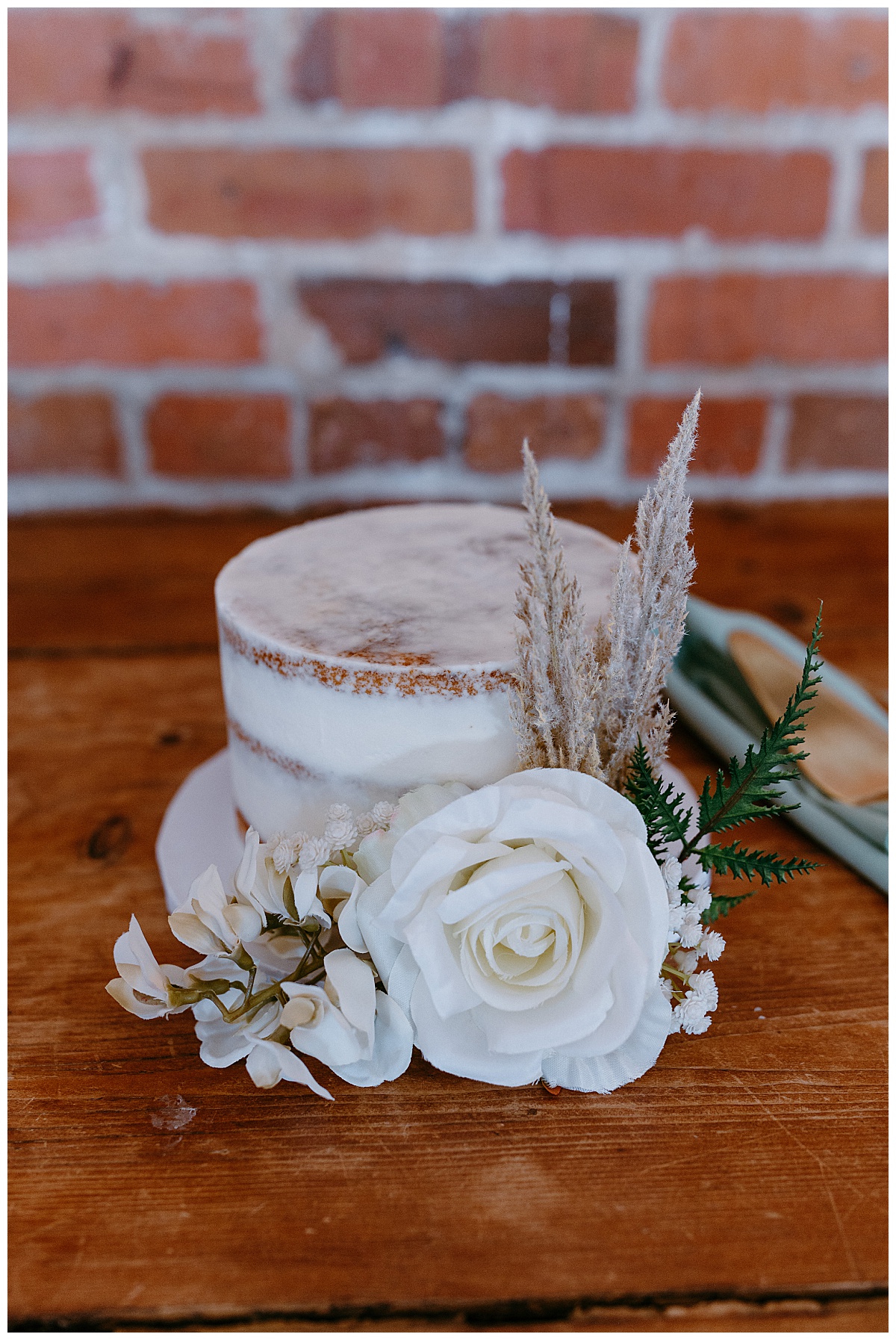 simple white wedding cake with florals sits on wooden table at River Room